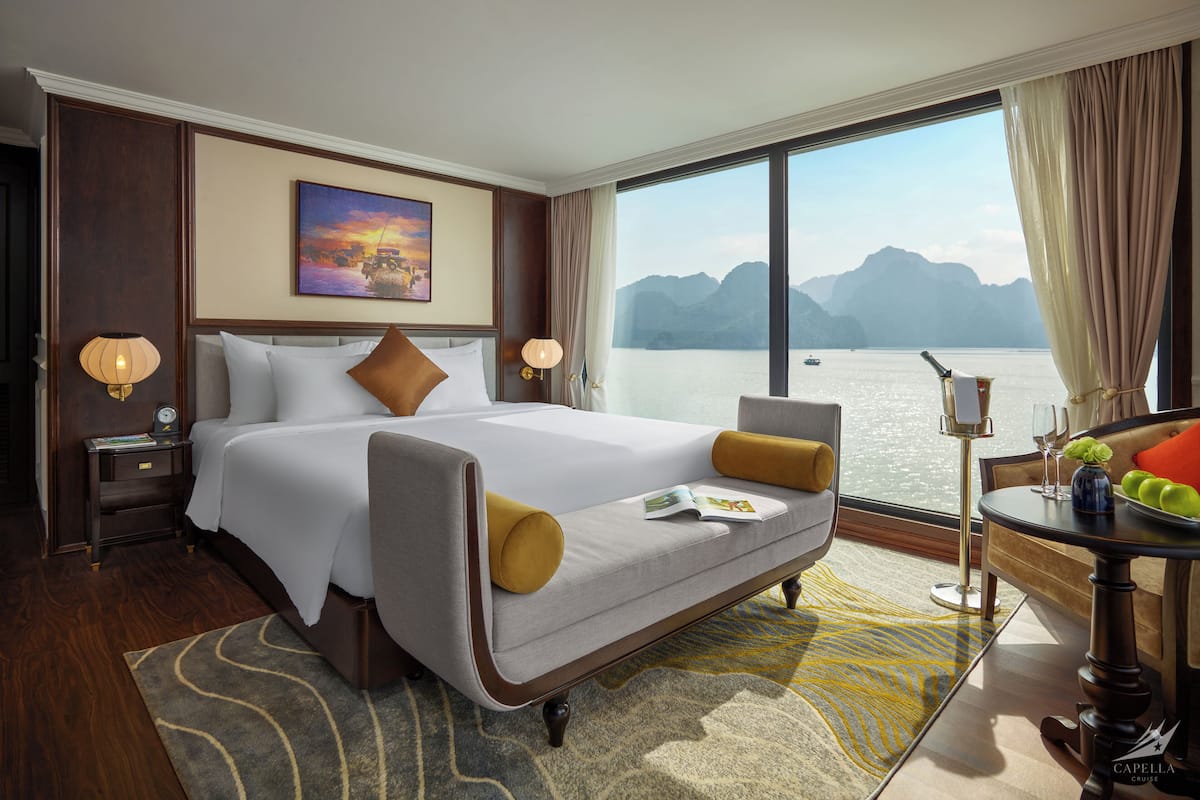 Hotelkamer met een groot bed, uitzicht op het water en een tafel met een vaas en appels.