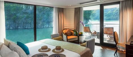 Habitación de hotel con una cama grande, un escritorio y un balcón con vista al agua.