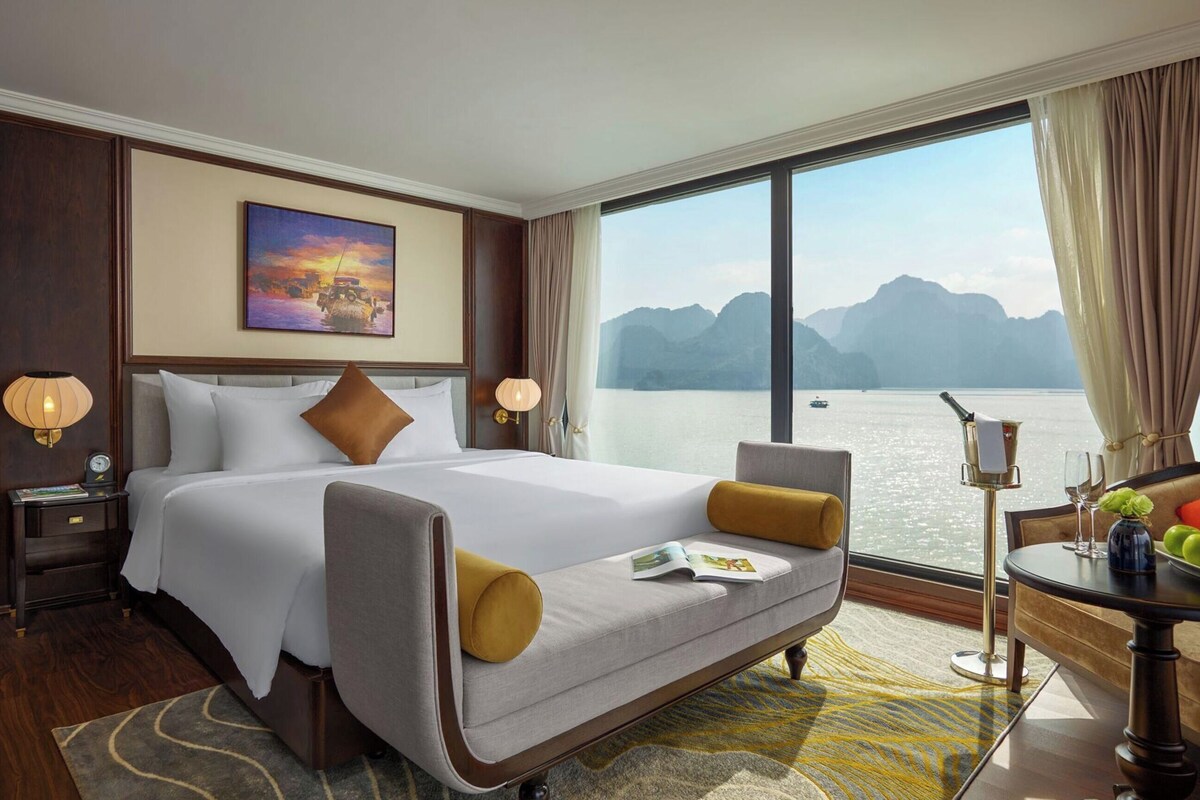 A hotel room with a large bed, a sofa, a desk with a lamp, and a view of a body of water.