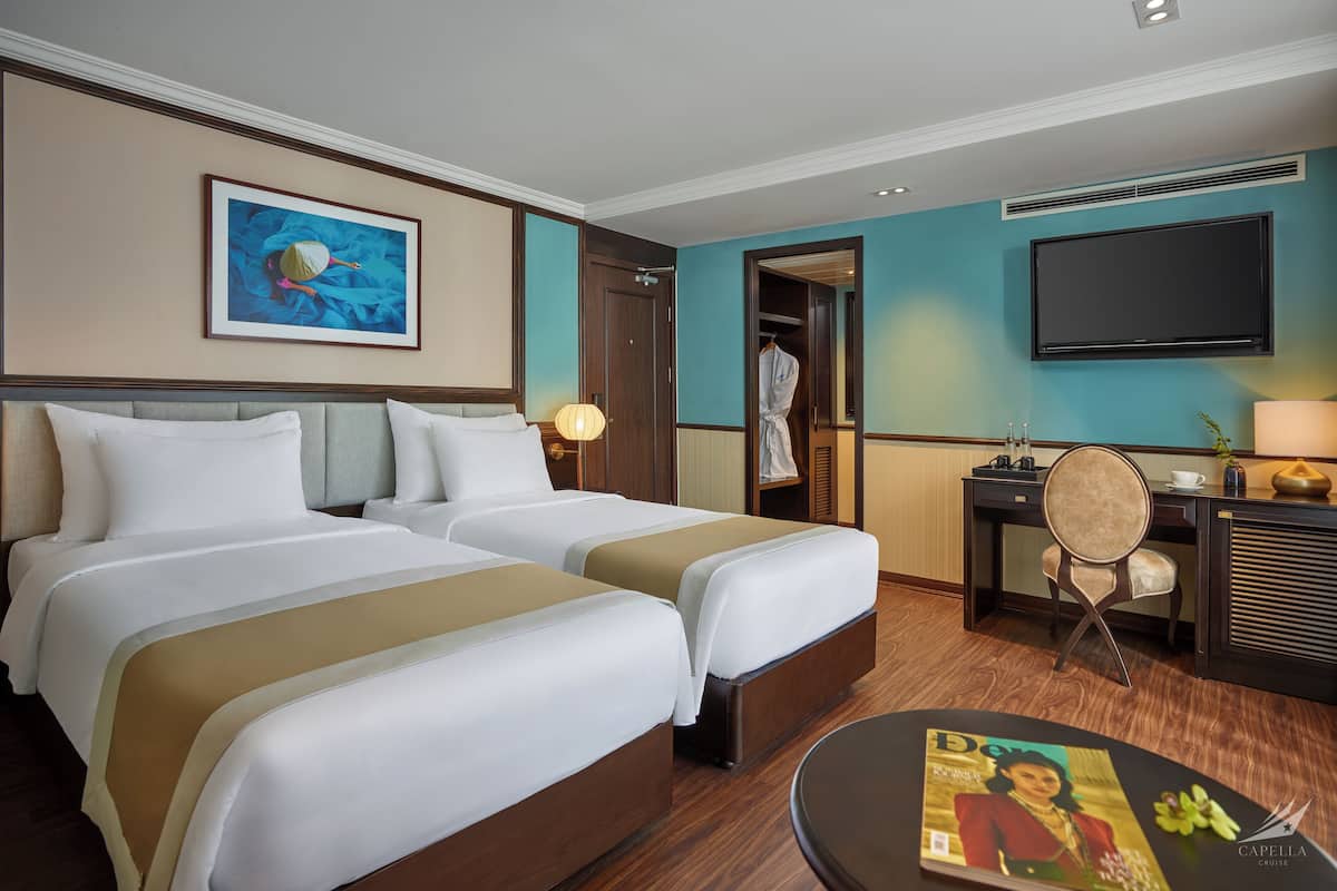Een hotelkamer met twee bedden, een bureau, een stoel, een televisie en een tijdschrift op de tafel.