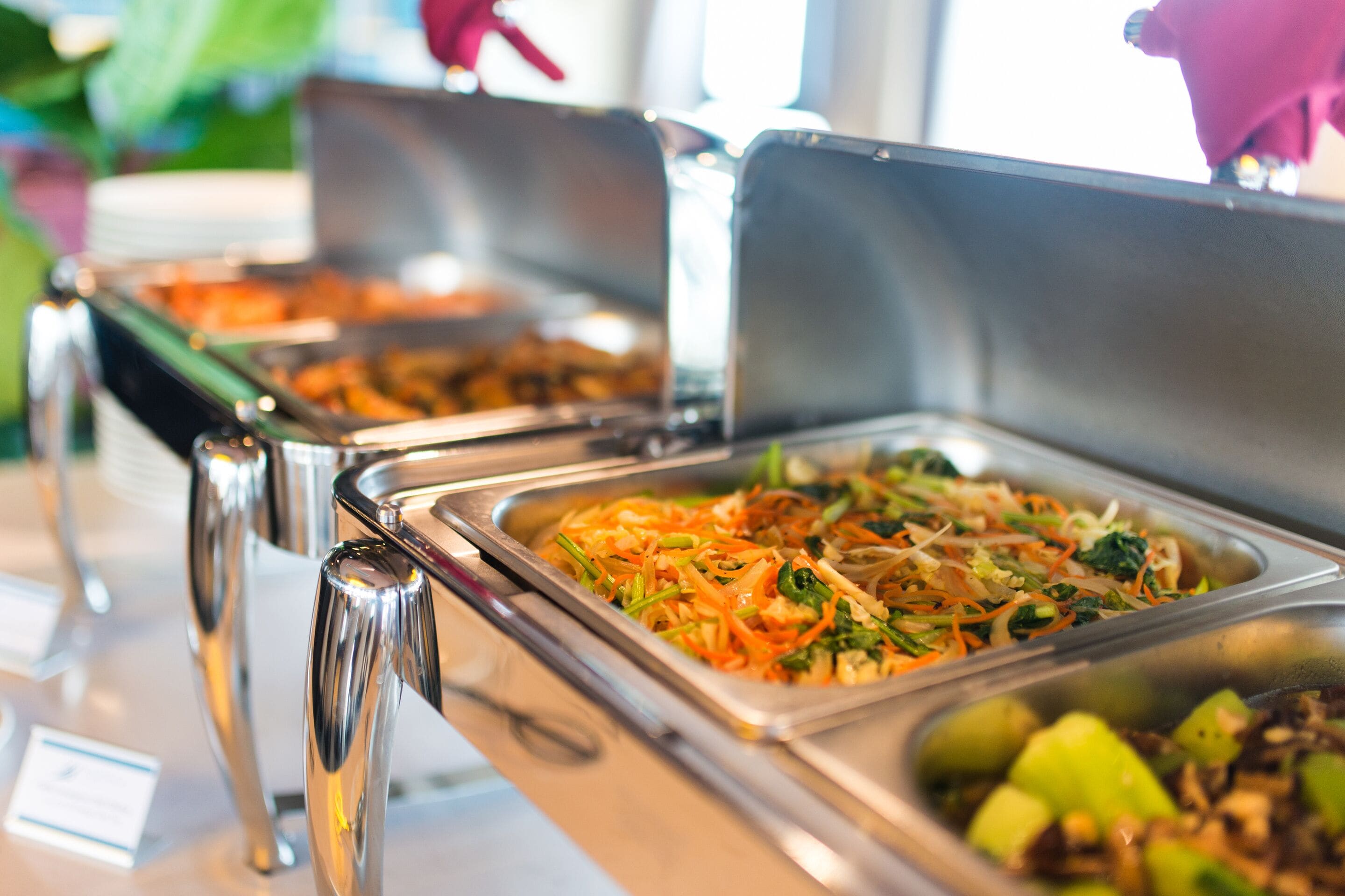 Un bufé con diversos platos, entre ellos ensaladas y verduras, dispuestos en bandejas metálicas.