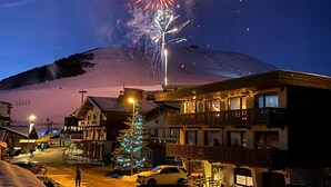 Un hotel con balcón y una colina nevada al fondo.