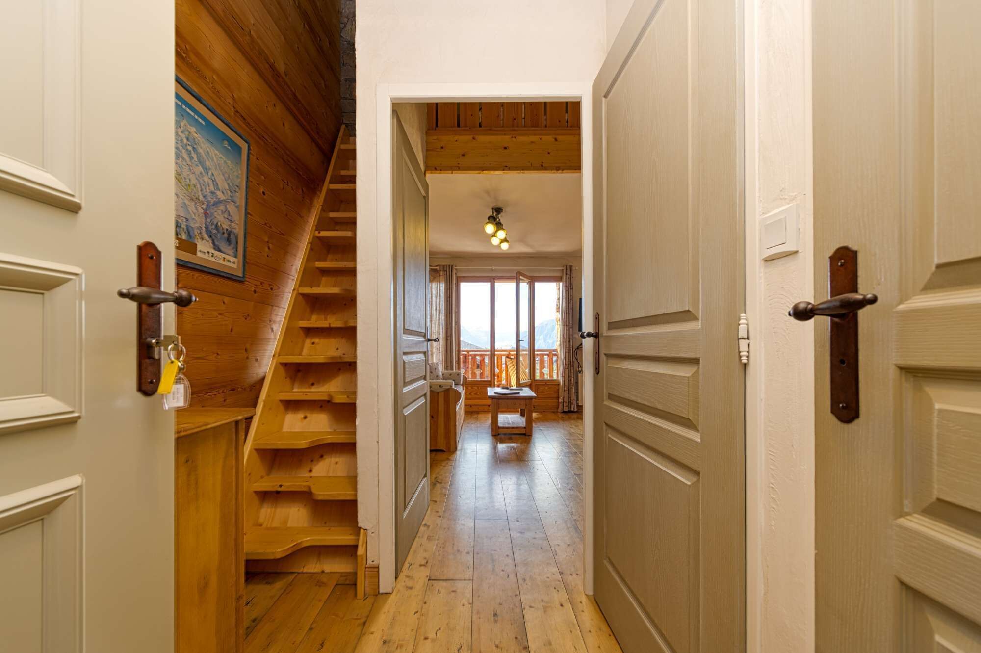 Una escalera de madera que conduce a un balcón con vistas, piso de madera y una puerta con la llave en la cerradura.