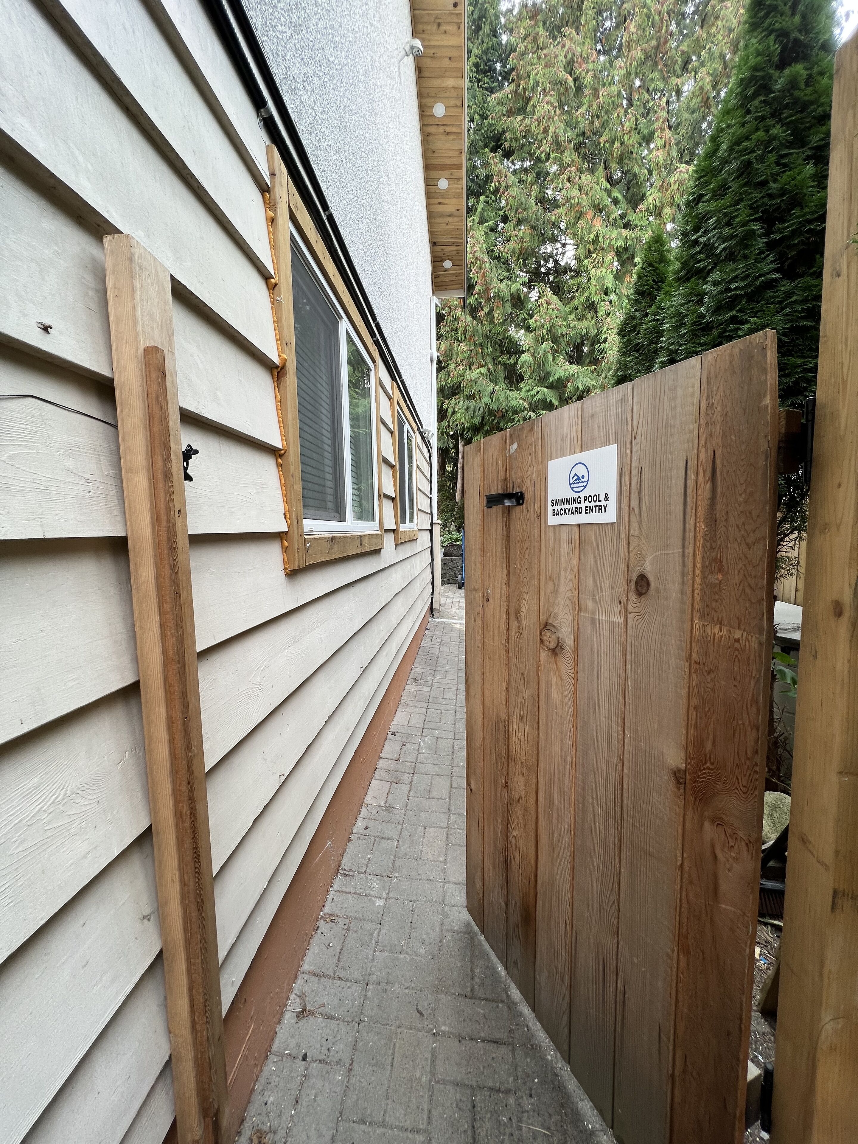 Una puerta de madera con un letrero que indica una piscina y acceso al jardín trasero.