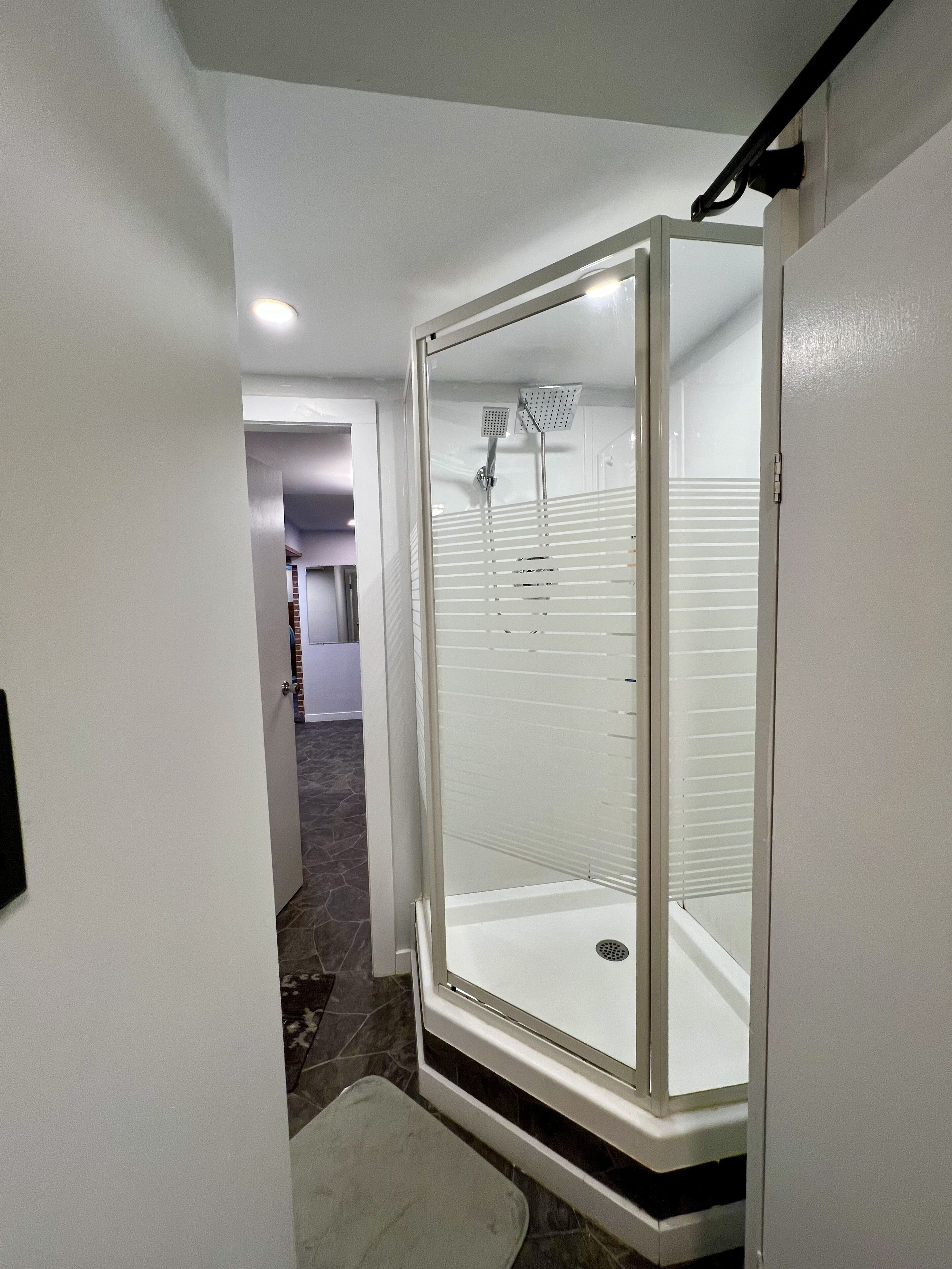 A walk-in shower with a glass door, a showerhead, and a drain.