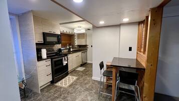 A compact kitchen with a microwave, stove, and sink. There is a dining table with chairs. The floor has a patterned tile design.