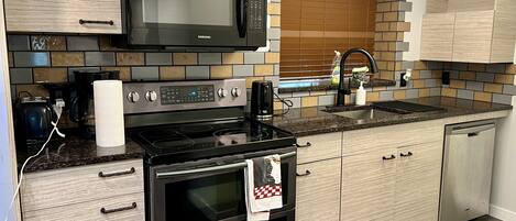 A modern kitchen with a microwave, stove, oven, and a sink with a wooden backsplash.