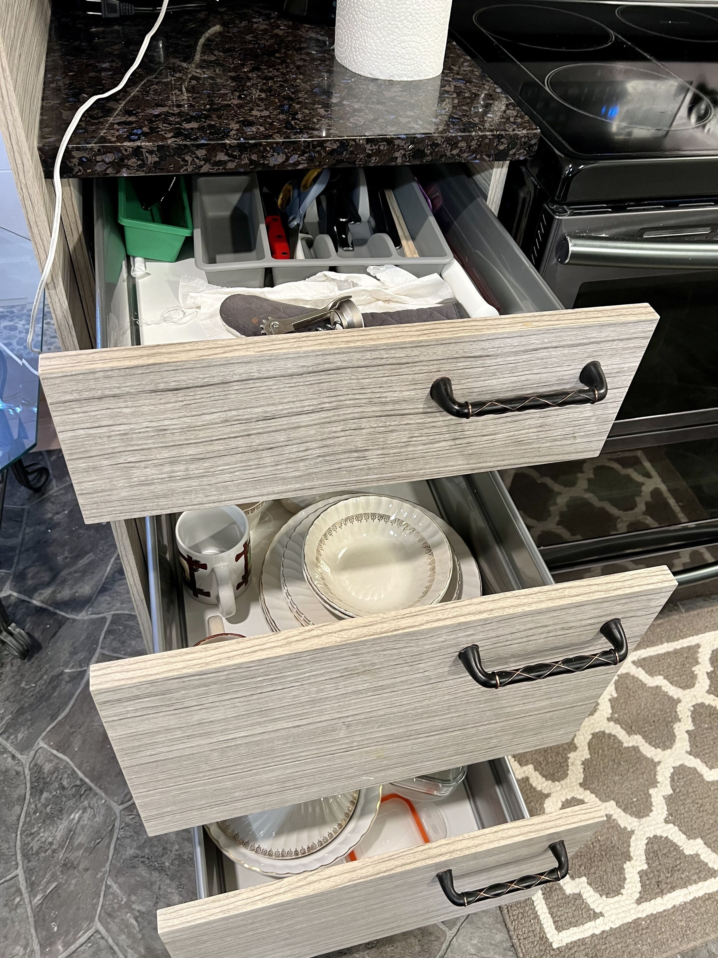 A kitchen counter with a paper towel holder, a coffee maker, and a drawer with kitchen utensils.