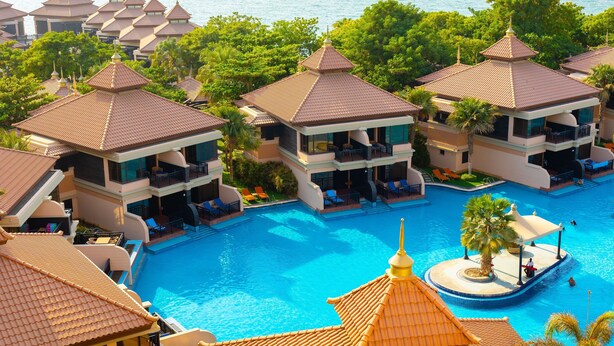 Een resort met meerdere bungalows boven het water, een centraal zwembad en weelderige begroeiing.
