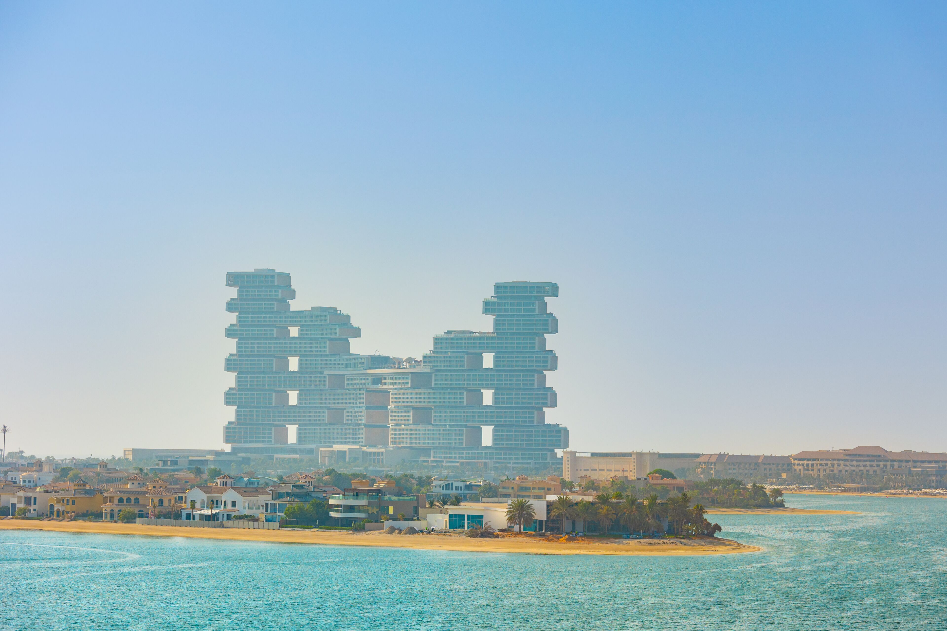 Un hôtel moderne au design original, caractérisé par une structure en étages superposés, situé près d’une plage aux eaux d’un bleu cristallin.