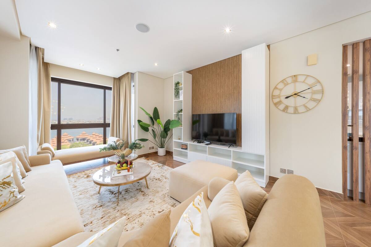 Een moderne woonkamer met een grote televisie, comfortabele zitplaatsen, een salontafel en een groot raam met uitzicht op de stad.