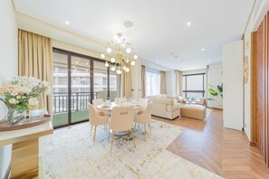 A modern living room with a dining area, large windows, and a chandelier.