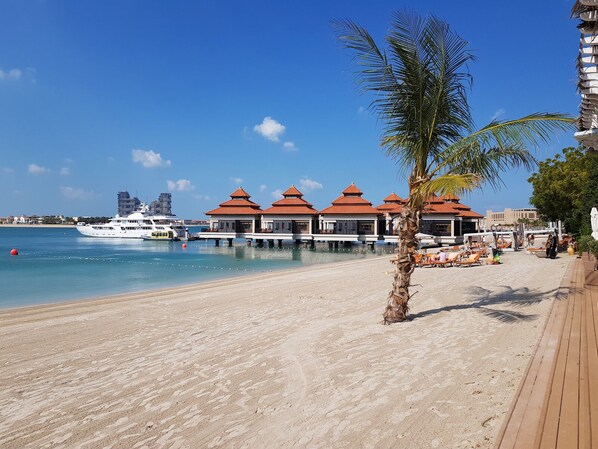 A beachside resort with overwater bungalows, a sandy beach, and a yacht docked near the water.