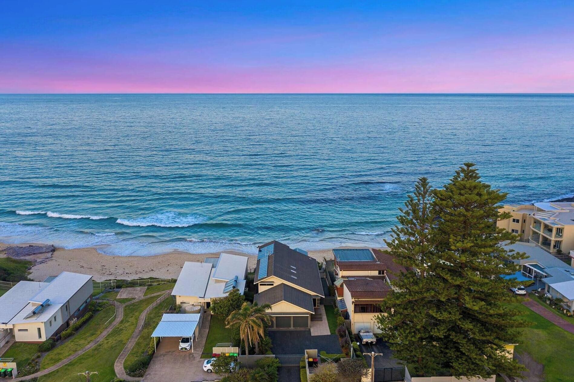 A coastal residential area with houses, a beach, and a clear sky.