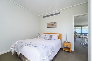 Relax in this serene bedroom with a large bed, bedside table, and a painting above, offering a view of the balcony with outdoor seating.