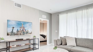 Een moderne woonkamer met een grijze bank, een ronde salontafel en een tv aan een gestreept wand.