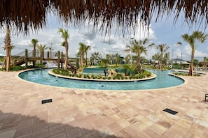 A swimming pool area with palm trees, a covered bridge, and a tiled walkway.