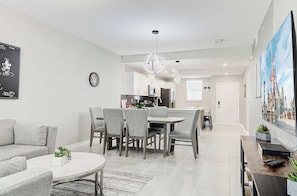 A modern living room with a dining area, kitchen, and a large window with a cityscape view.