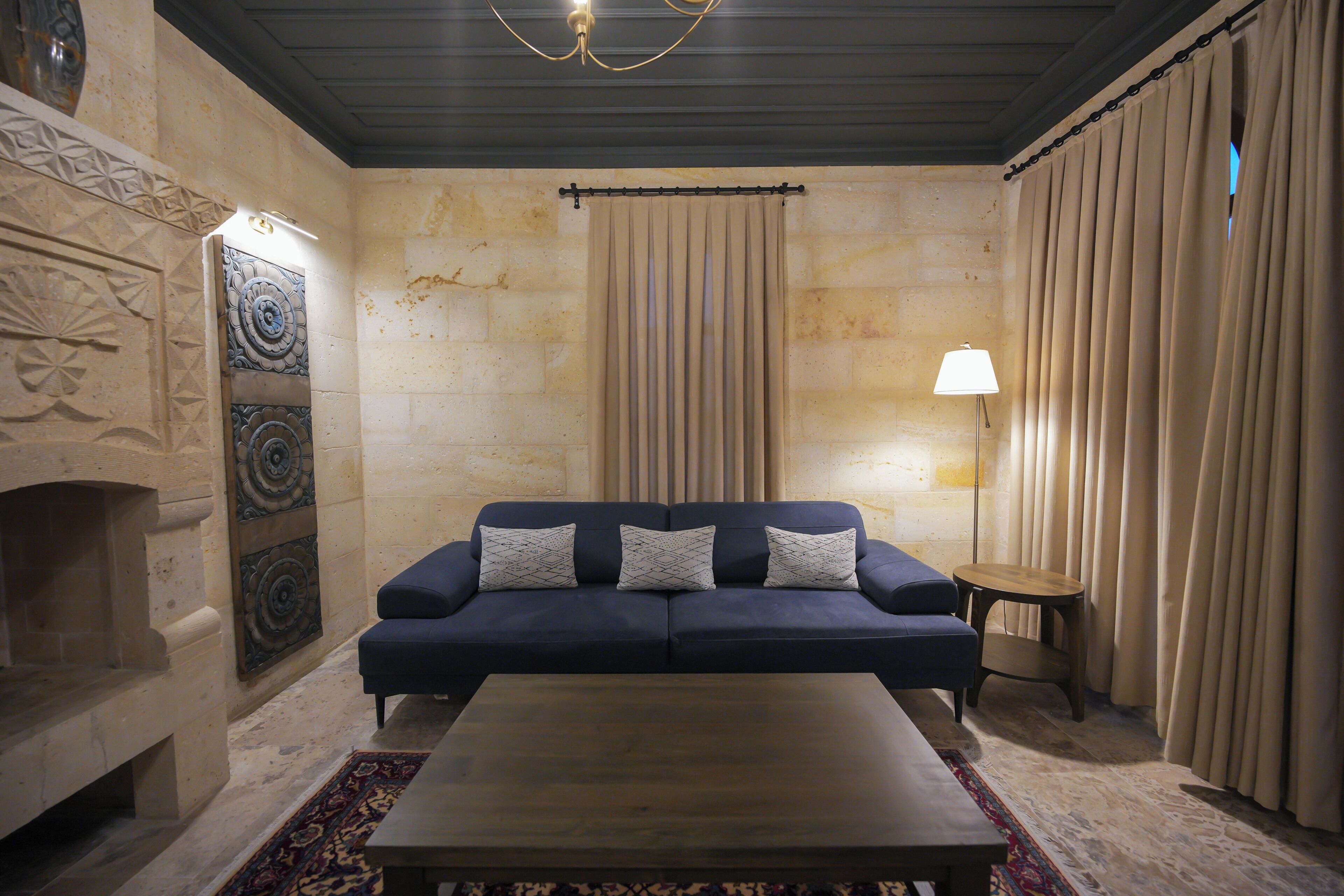 A room with a blue sofa, a wooden coffee table, a patterned rug, a wall-mounted lamp, and a fireplace.