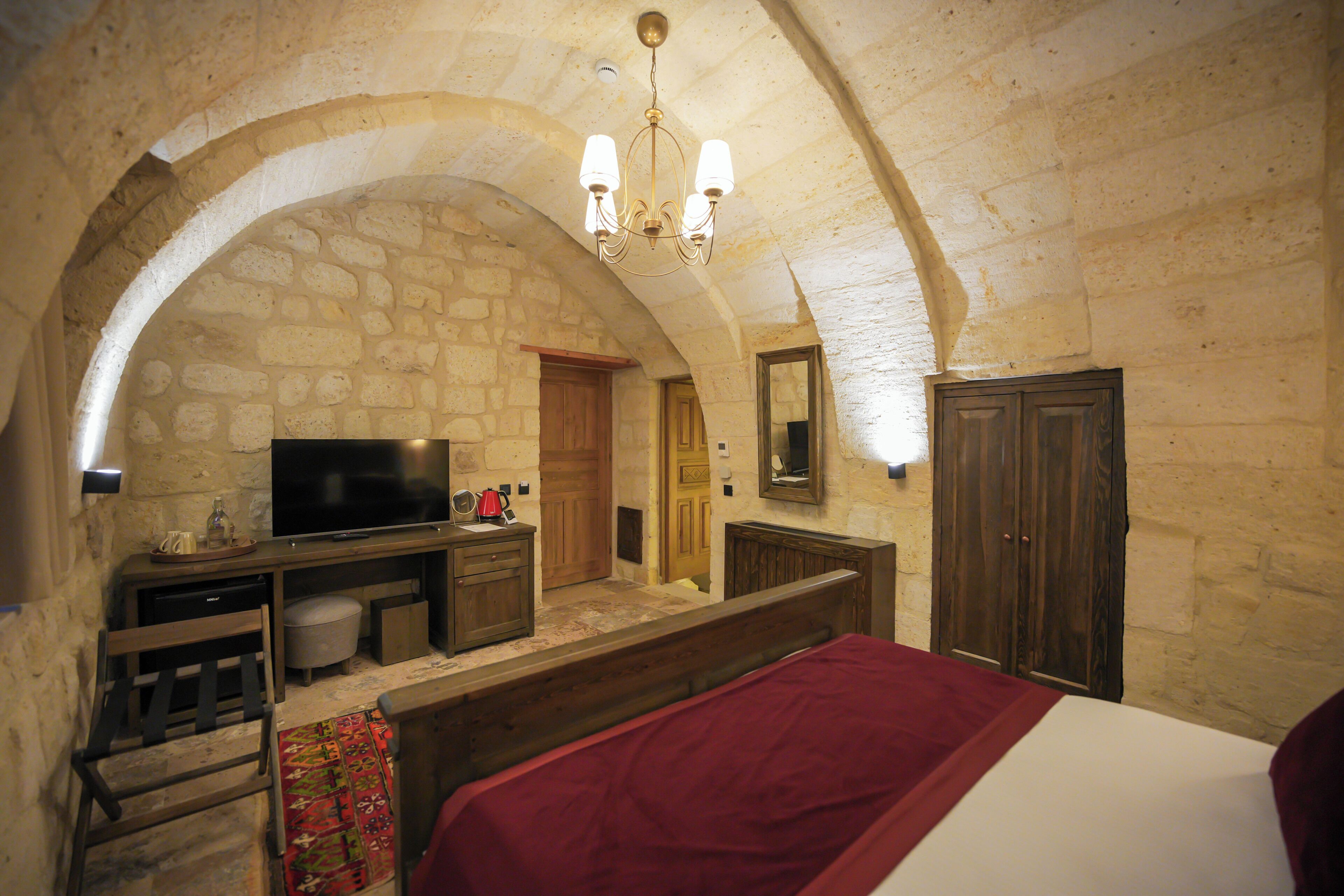 A stone-walled room with a television, wooden furniture, and a bed.