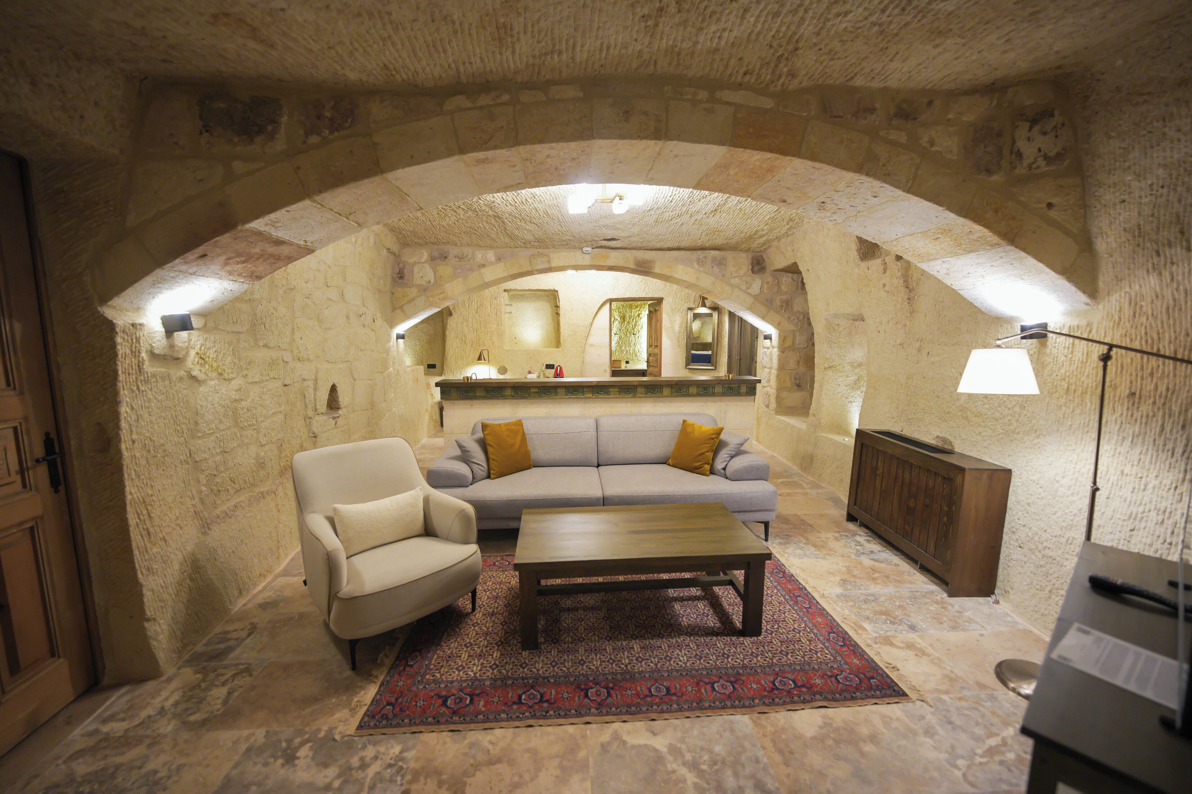 An arched stone room with a sofa, armchair, coffee table, and a rug.