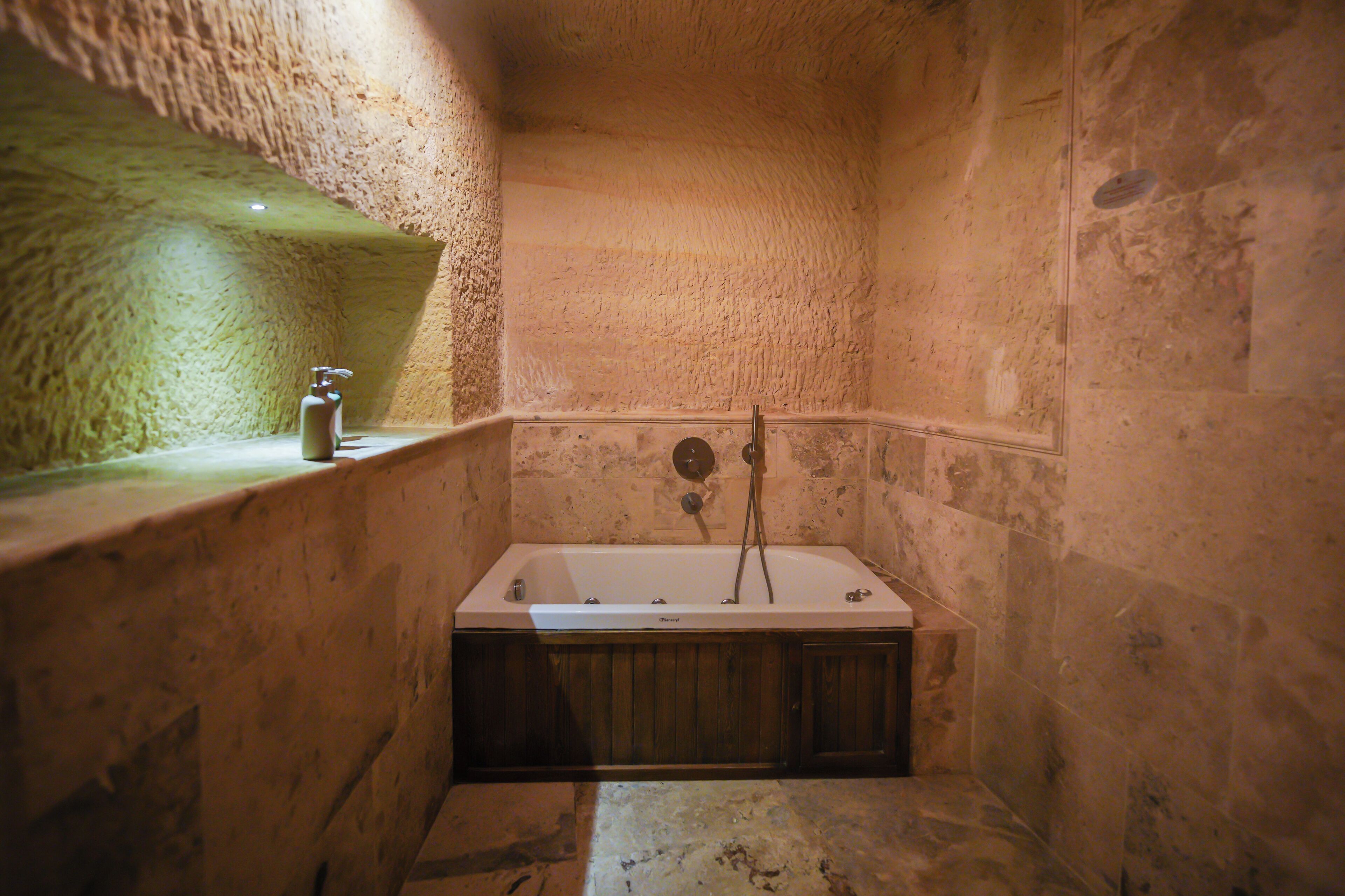 A stone-walled bathroom with a freestanding bathtub, a faucet, and a bottle of soap.