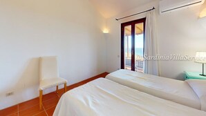 A room with two beds, a chair, a window with curtains, and a view of the sea. - Apartment Dream - Cala Granu (Arzachena)