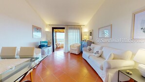A modern living room with a glass dining table, white sofas, a TV, and a view through a large window. - Apartment Dream - Cala Granu (Arzachena)