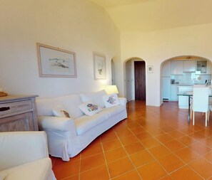 A spacious living area with a white sofa, a television, and a kitchen in the background.