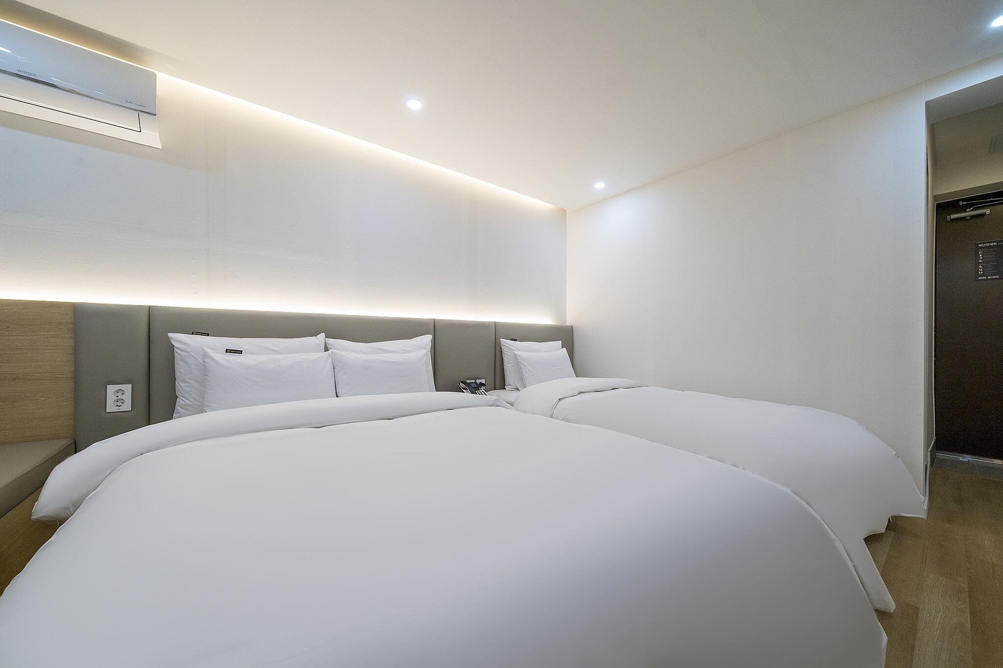 Una habitación de hotel moderna con una cama grande, cabecera con iluminación integrada y un equipo de aire acondicionado instalado en la pared.