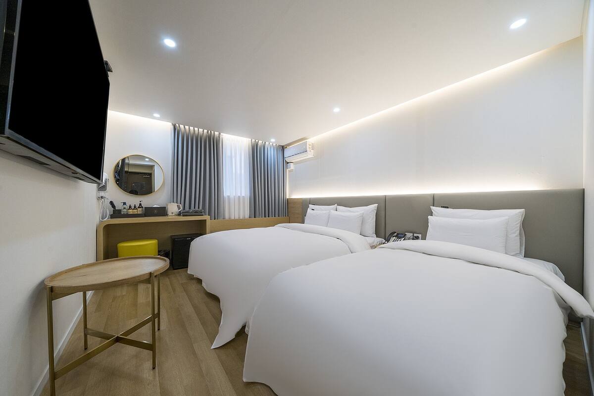 Ett hotellrum med två sängar, ett skrivbord, en stol, en TV och en spegel.