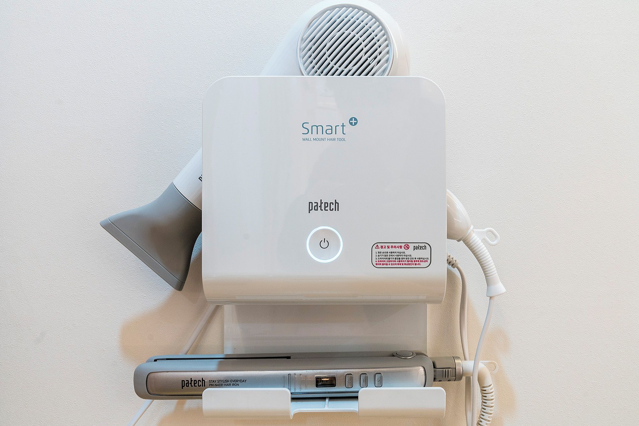 A wall-mounted hair tool with a power button, a hair iron, and a charging cable.