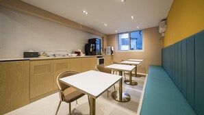 A modern kitchen with wooden cabinets, a coffee machine, and a microwave. There are tables and chairs arranged for dining. - Browndot Hotel Namchuncheon (Chuncheon)