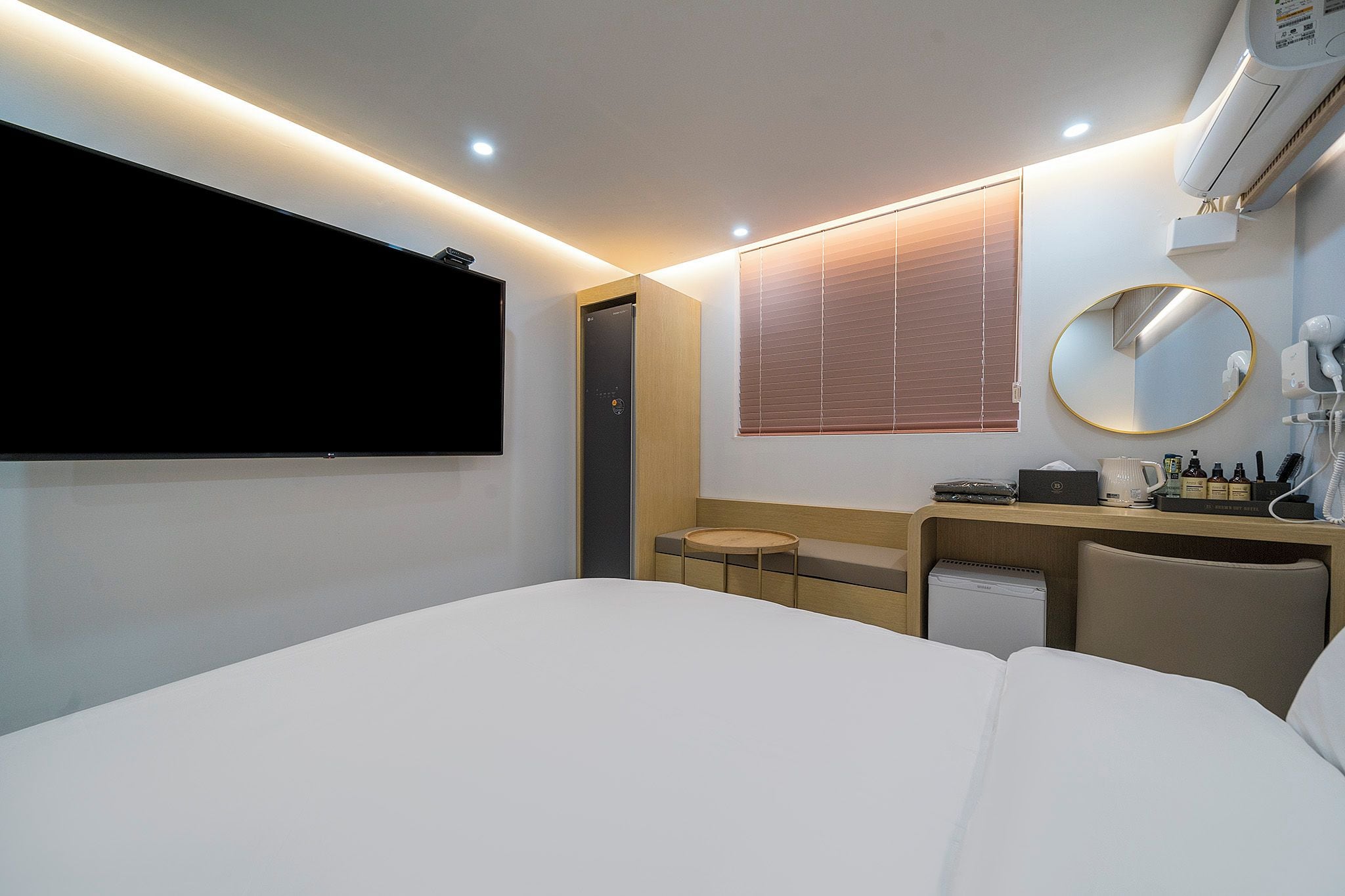 A hotel room with a bed, a desk, a mirror, and a TV.