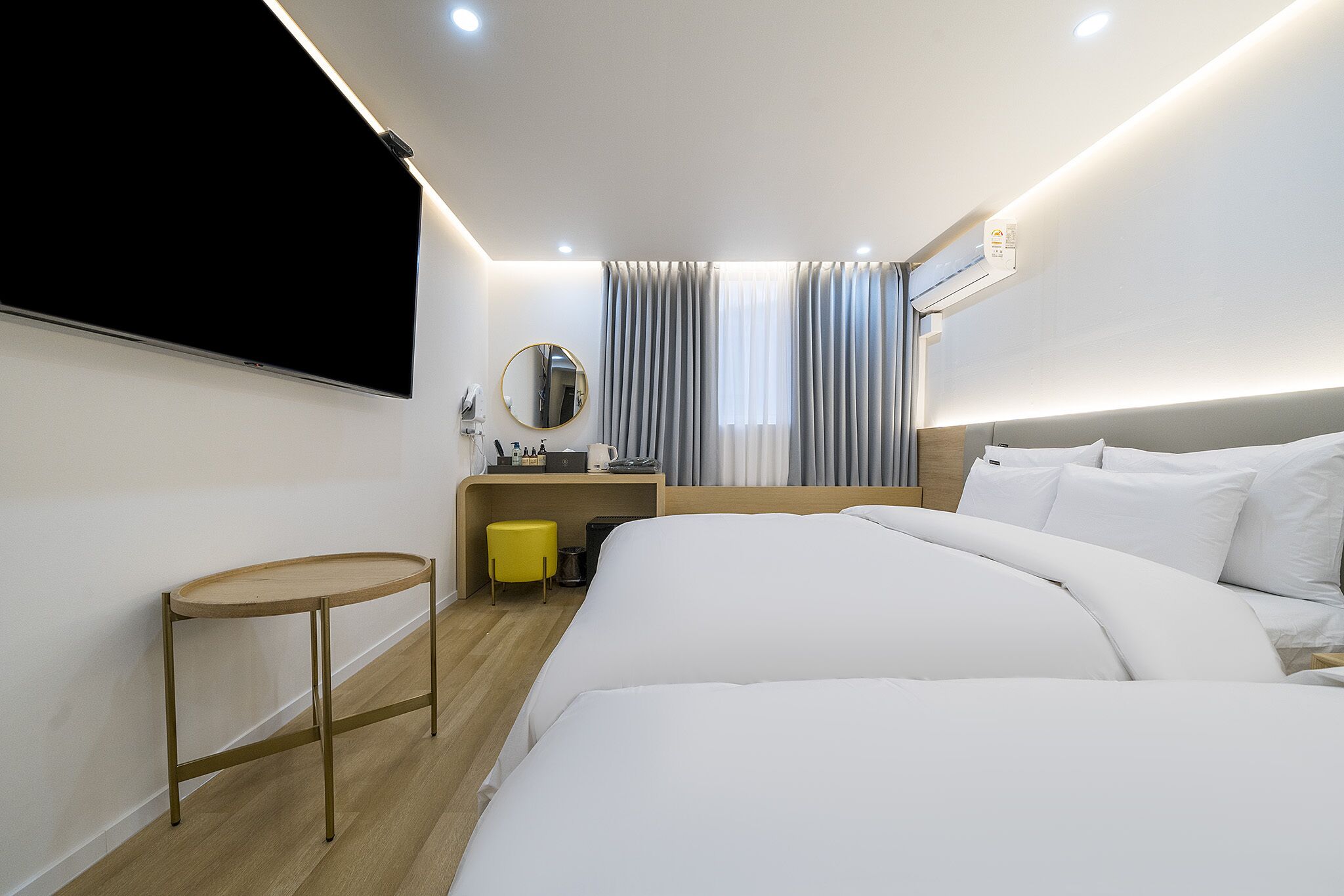 A hotel room with a bed, a small desk with a chair, a TV mounted on the wall, and a window with curtains.