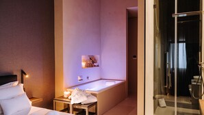 A modern hotel room with a large bed, a separate bathroom with a bathtub, and a glass-enclosed shower area. - Suite1212 Bandiera  (Monopoli)
