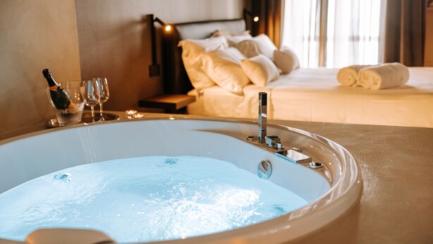 A large bathtub with a faucet, a bottle of champagne, and two glasses on a tray. - Suite1212 Bandiera  (Monopoli)
