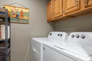 A laundry room with a stacked washer and dryer, wooden cabinets above, and a shelf with folded clothes.