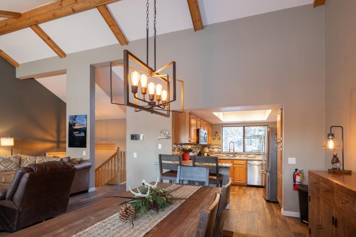A modern kitchen with wooden cabinets, a dining area with a wooden table, and a hanging light fixture.