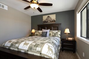 A bedroom with a bed, two bedside tables with lamps, a ceiling fan, a wall-mounted artwork, and a window.