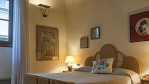 A bedroom with a wooden bed frame, a bedside table with a lamp, and a large window with curtains. - San Miniato Apt - Luxury Apartments at 20 steps from Duomo; Elevator equipped. (Firenze)