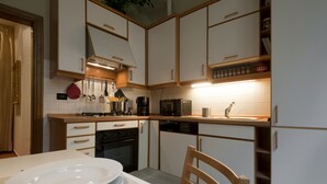 A kitchen with white cabinets, a stove, microwave, and a sink. There is a dining table with plates and a chair. - San Miniato Apt - Luxury Apartments at 20 steps from Duomo; Elevator equipped. (Firenze)