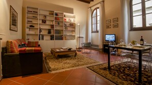 A living room with a sofa, coffee table, and a dining area with chairs and a table set for two. There is a bookshelf filled with books and decorative items. - San Miniato Apt - Luxury Apartments at 20 steps from Duomo; Elevator equipped. (Firenze)