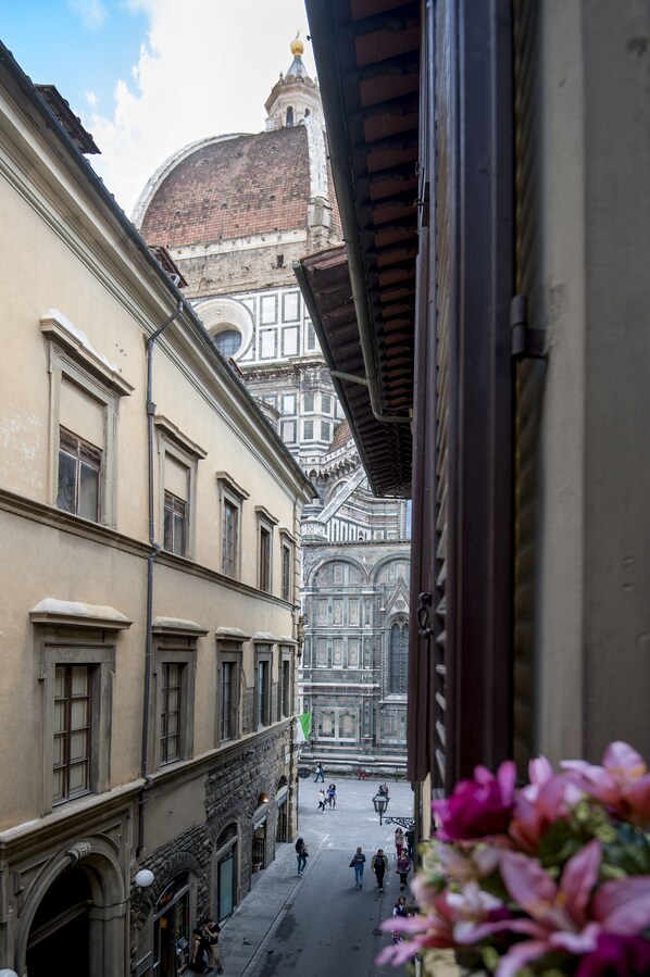 Eine enge Straße mit historischen Gebäuden, einer markanten Kuppel und Blick durch ein offenes Fenster.