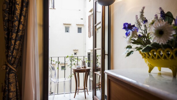 A balcony with a clear view of the street, a small table with a chair, and a vase of flowers on the windowsill. - San Miniato Apt - Luxury Apartments at 20 steps from Duomo; Elevator equipped. (Firenze)
