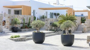 A modern building with white walls and stone accents, featuring large potted plants and a stone staircase. - Brilliance of Mykonos (Mykonos)
