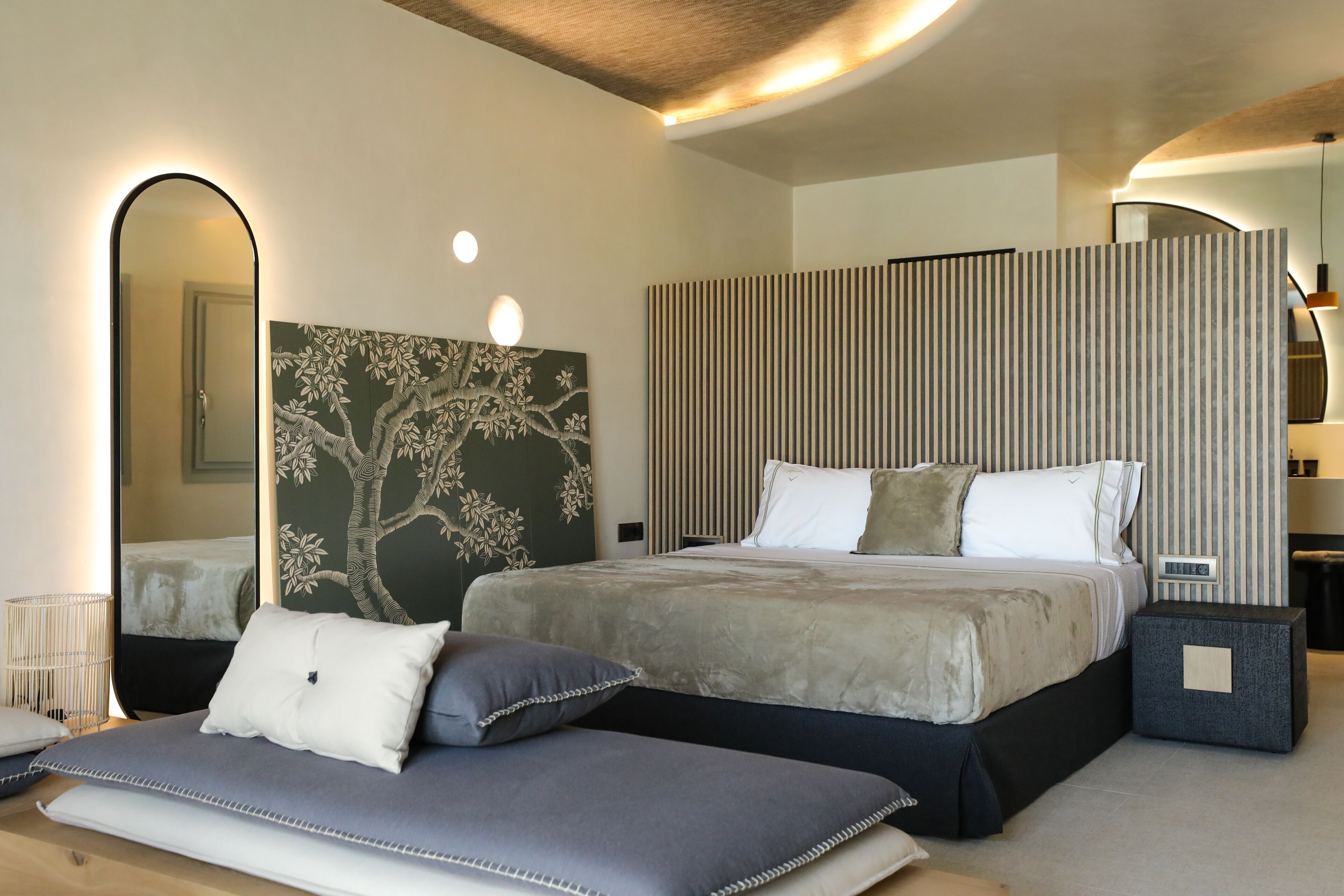 A modern bedroom with a large bed, a bedside table, a mirror, and a wall-mounted artwork.