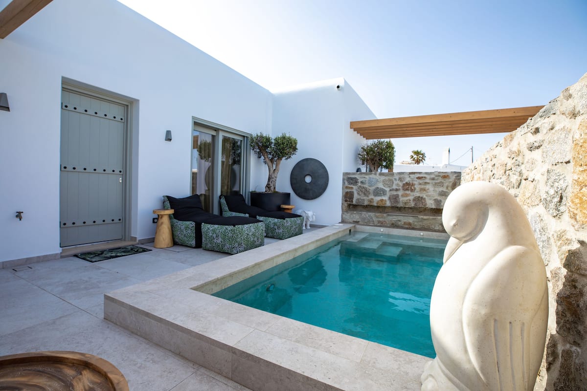 A modern outdoor pool area with a stone wall, a statue, and outdoor seating.