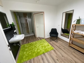 A modern bathroom with a sink, shower, and a green rug.