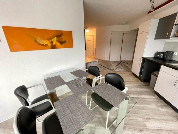 A modern dining area with a glass table, black chairs, and a large abstract painting on the wall.